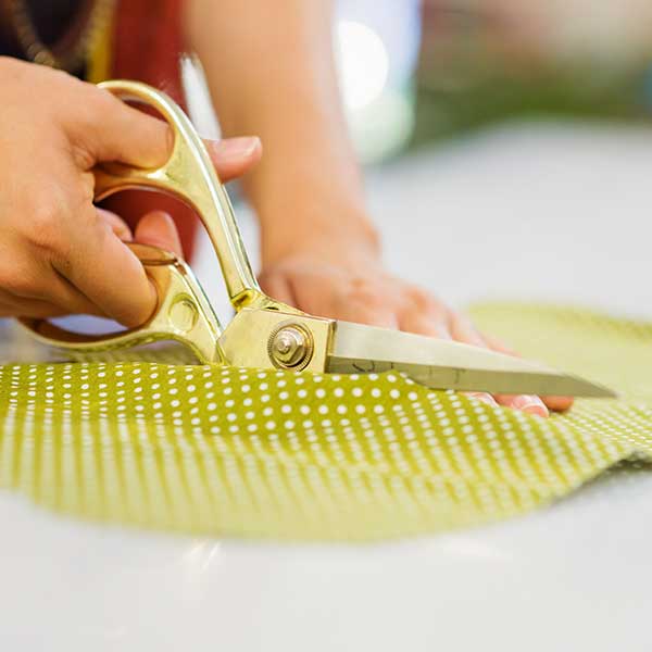 Someone with gold-handled fabric scissors cutting lime green fabric with white polka dot pattern