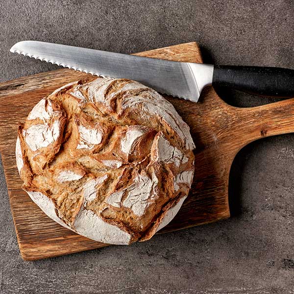 Top View of a large round loaf of soda bread laying on a wood cutting board with a serrated knife laying next to it